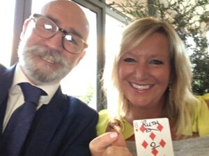 Woman holding a playing card and a bent soin. Accompmnaied by a magician. Magic Frank