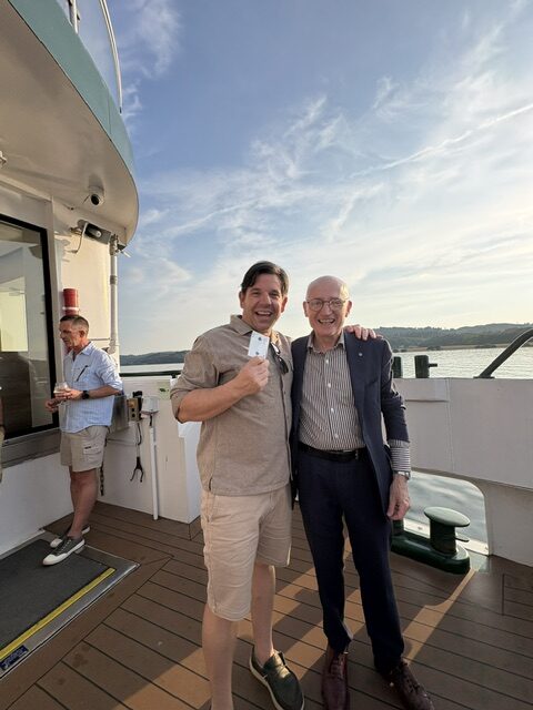 magician, magic frank. and a guest on baord a steamer on lake Windemere. The guest is holding a playing card. both men are smiling.